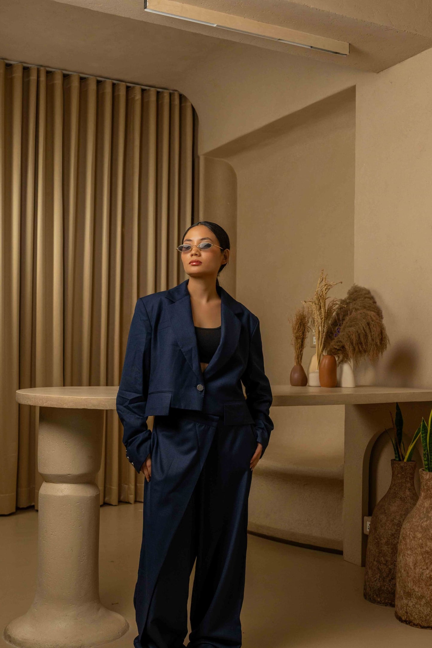Woman in a navy blue outfit standing in a room with beige walls and decorative elements.