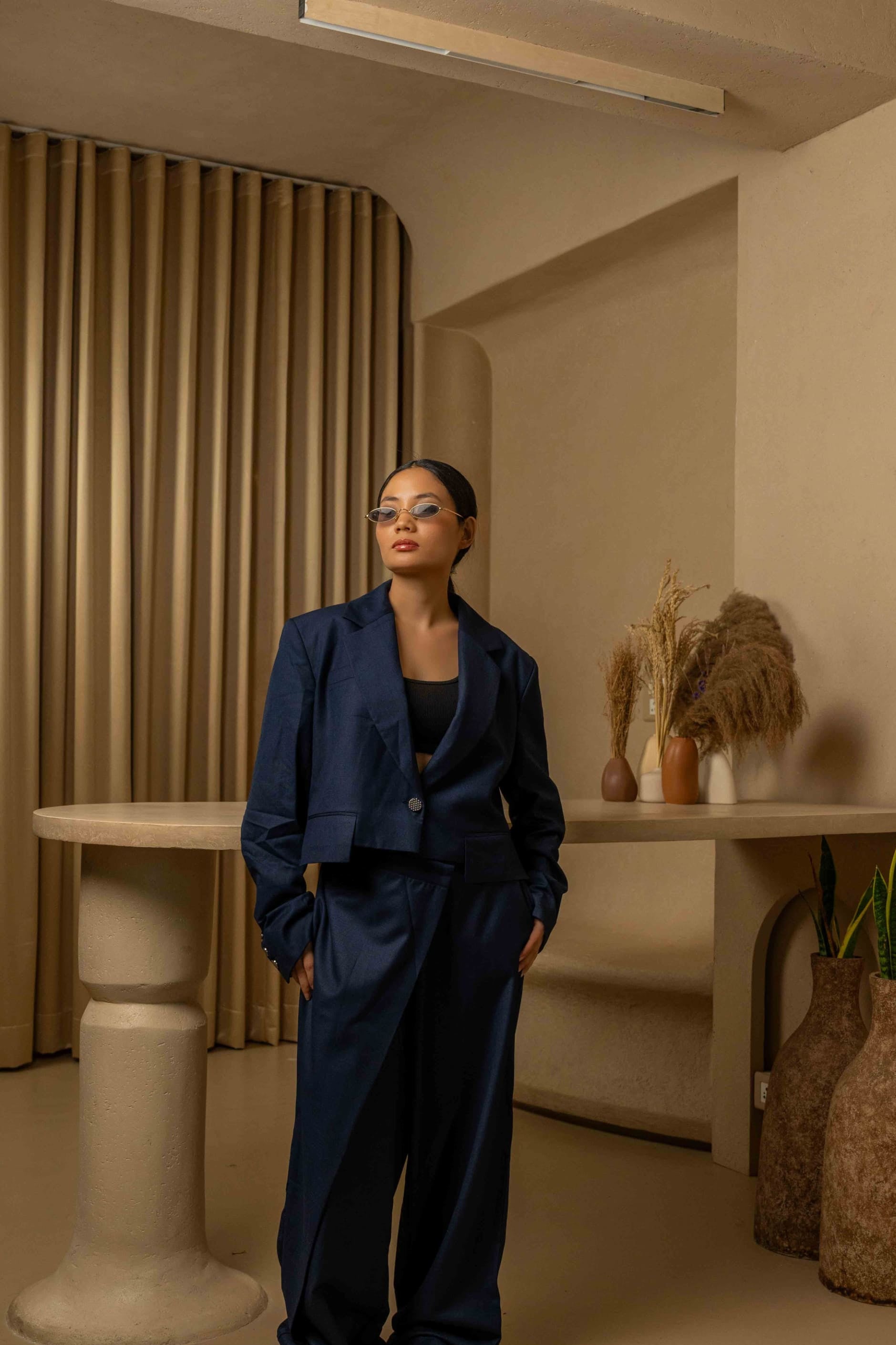 Woman in a navy blue outfit standing in a room with beige walls and decorative elements.